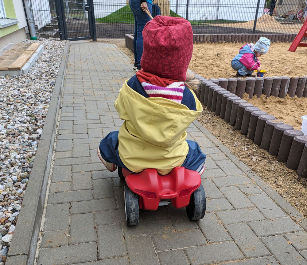 Ein kleines Kind sitz in einem Spielauto und fährt einen Weg entlang